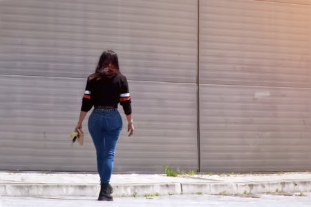 A young woman in jeans and a black T-shirt is walking along the street.の写真素材