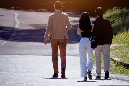 Back view of young couple holding hands while walking on road in parkの写真素材