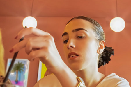 Beautiful young woman applying makeup in front of a mirror in a beauty salon