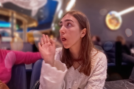 Surprised young woman sitting in a cafe and looking at the camera.