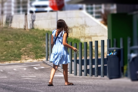 A little girl in a blue dress is walking along the street.の写真素材
