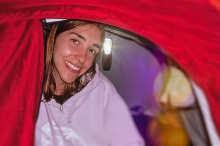 Young woman camping in tent at night, she is smiling and looking at cameraの写真素材