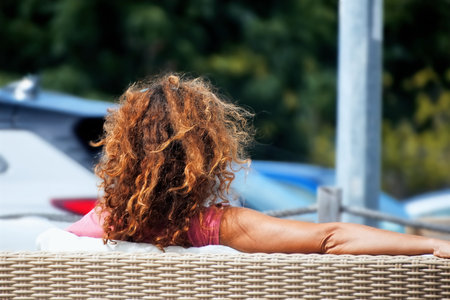 Rear view of young woman with curly hair sunbathing on a sun loungerの写真素材