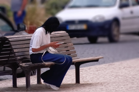 A woman sitting on a bench in the street and using her mobile phoneの写真素材