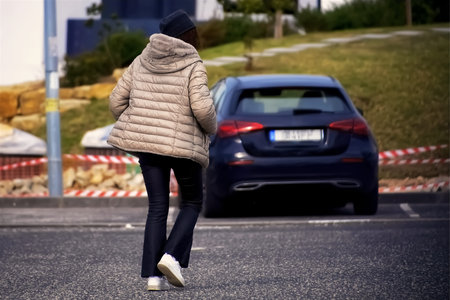 Rear view of a woman walking on the road with a car in the background