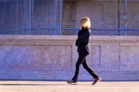 Blonde woman in a black jacket walking on the street at sunset