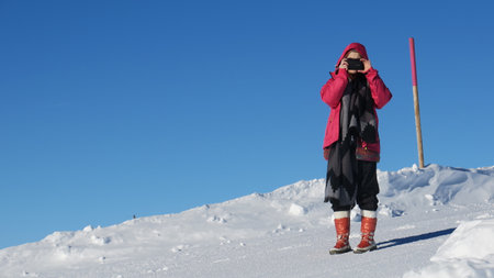 Woman in Red Jacket Taking Photo on Snowy Mountain Peak