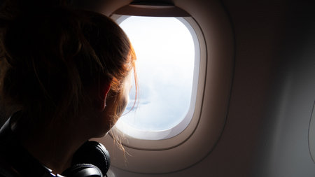 Woman looking out airplane window at clouds