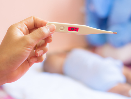 Thirty-nine degrees on medical thermometer in mother hand, and infant asleep on White mattress....