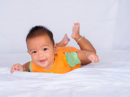 Asian infant lie on the stomach, Wearing an orange shirt On a white cloth.の写真素材