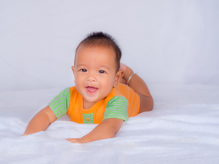 Asian infant lie on the stomach, Wearing an orange shirt On a white cloth.
