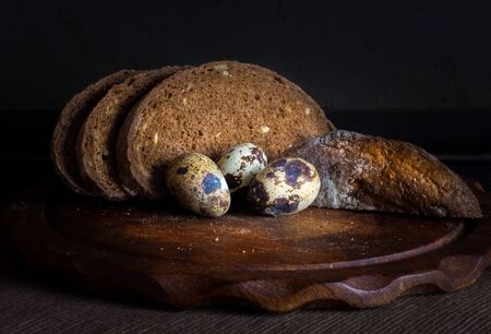 Fresh bread on wooden table,vintage filter, Traditional black rye-bread on dark background,   sliced bread and quail eggs, vintage still lifeの写真素材