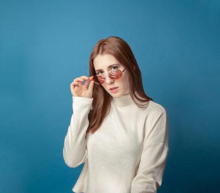 redhead woman looking over her glasses in a blue backgroundの写真素材