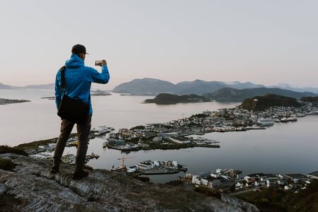 Traveller is taking pictures of scenic norwegian city view from the mountain. Travel and hiking concept. Shot during the blue hour. の写真素材