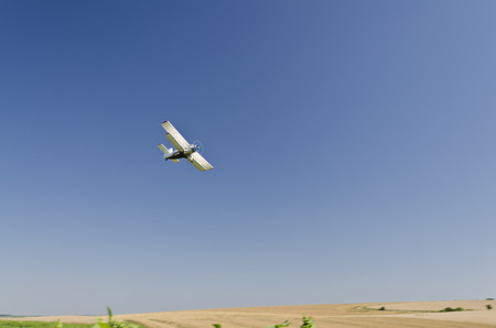 An agricultural crop duster flying low over a sunflower field, spraying chemicals