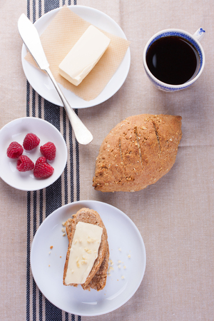 Homemade oatmeal bread on a wooden table with coffee, butter and raspberries for breakfast. Topviewの写真素材
