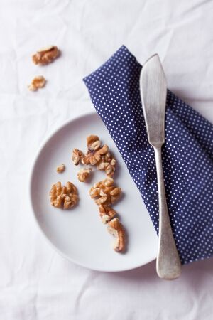 Walnuts on a white ceramic plate with blue napkin and knife. Top viewの写真素材