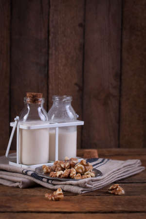 Homemade walnut nut milk in glass bottles on a wooden backgroundの写真素材