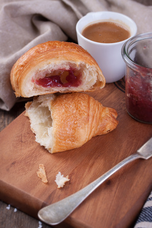 Closeup of croissant with jam and coffee on a wooden backgroundの写真素材