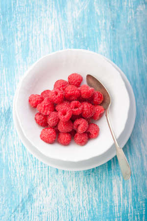 Fresh raspberries in a white ceramic bowl with metal spoon. top view