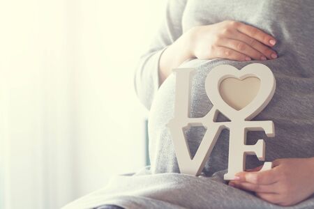Young pregnant woman holds wooden letters LOVE. Love concept. Horizontal with copy space