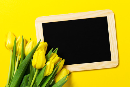 Fresh beautiful yellow tulips on yellow colorful background with chalkboard. Spring concept. Horizontal, top view with copy space. の写真素材