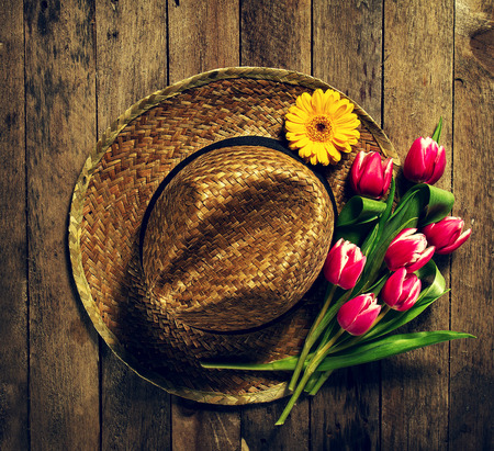 Straw hat with bunch of purple tulip flowers on vintage wooden table. Spring, summer or garden concept background, top view.の写真素材