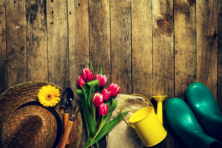 Gardening tools, flowers, watering can, rubber boots and straw hat on vintage wooden table. Spring, summer or garden concept background with free text space.の写真素材