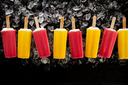 Tasty cold fresh appetizing ice cream on stick on ice cubes on dark background with copy space. Top View.の写真素材