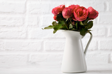 Background of white metal pitcher with fresh delicate roses on white brick wall background.の写真素材