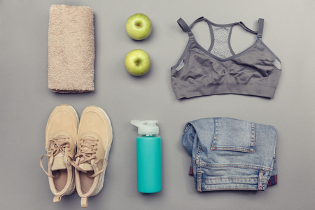 Top view of sneakers, clothes, apple, bottle of water, and green apples on gray background.の写真素材