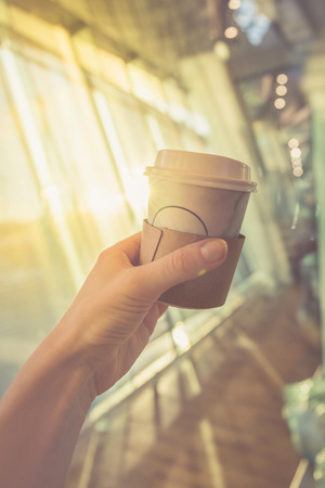 Hand of unrecognizable person holding paper cup at window in sunny day.の写真素材
