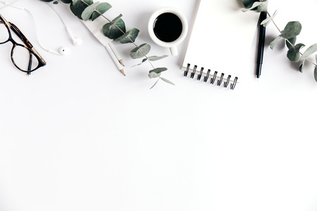 Top view of white table with clear notepad, glasses, headphones and green plant.の写真素材