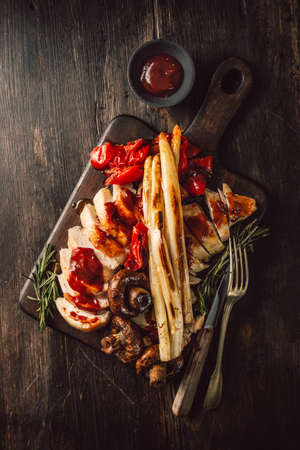 From above chicken breast with vegetables and sauce on wooden board. の写真素材