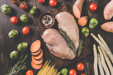 From above uncooked chicken breasts and fresh vegetables on wooden table. の写真素材