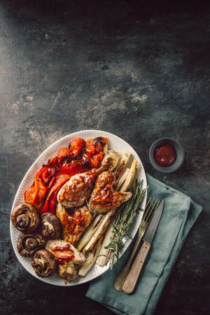 From above dish with chicken and vegetables served with sauce on dark rough background.