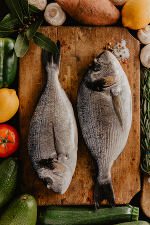 Top view of fish on rough board with spices and different vegetables.の写真素材