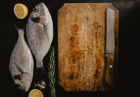 Top view of two dorado fish with lemon and rosemary at cutting board.の写真素材