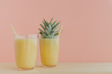 Two glasses filled with freshly made pineapple smoothie and served with colorful straws. 