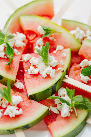 Watermelons slices on sticks served with pieces of feta cheese and mint leaves.の写真素材