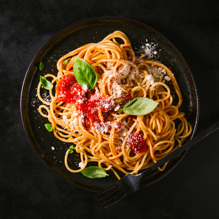Tasty appetizing classic italian spaghetti pasta with tomato sauce, cheese parmesan and basil on plate on dark table. View from above, top viewの写真素材