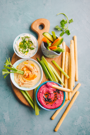 Appetizing vegetarian healthy dips sauces in small bowls with cut vegetables on cutting board. View from above. Healthy detox weight loss concept.の写真素材
