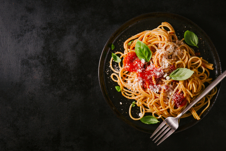 Tasty appetizing classic italian spaghetti pasta with tomato sauce, cheese parmesan and basil on plate on dark table. View from above, horizontalの写真素材
