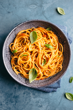 Tasty appetizing pasta served with tomato sauce, fresh tomatoes, basil and cheese in bowl on blue table. View from aboveの写真素材