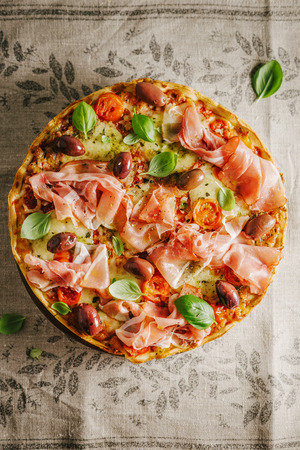 Appetizing classic traditional italian pizza with cheese, ham and vegetables on rustic textile. View from aboveの写真素材