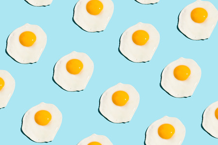 Fried eggs, scrambled eggs on blue background in food pattern. View from above. Food fashion...