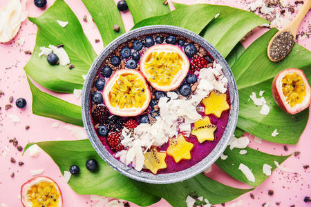 Tasty appetizing smoothie acai bowl made from blackberries and wild berries, decorated with cut passion fruit, coconut flakes, and cacao nibs. Served in bowl. Healthy life clean eating concept.の写真素材