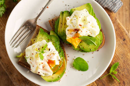Fresh sandwich with avocado and poached egg on bread. Served on plate. Closeup
