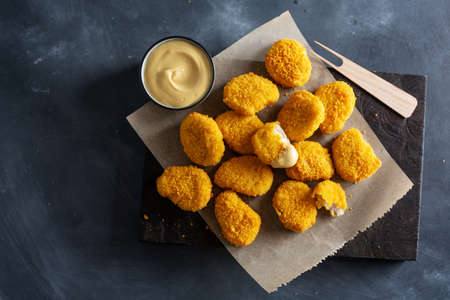 Tasty appetizing crispy chicken nuggets served on wooden board with mustard on dark background.の写真素材