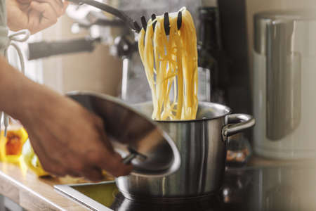 Man cooking pasta spaghetti at home in the kitchen. Home cooking or italian cooking concept.の写真素材